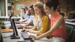 Estudiantes en un aula de informática aprendiendo sobre inteligencia artificial. La imagen representa cómo Enseñar IA de forma práctica con el uso de computadoras y tecnología educativa.